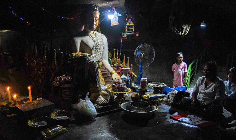 A candlelit statue of Lok Yeay Mao inside the caves near Kampong Trach, with a fortune teller and family seated nearby