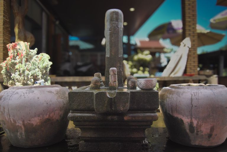 A stone linga offering at a Lok Yeay Mao shrine on the Kampot to Phnom Penh highway, flanked by two ceramic jars