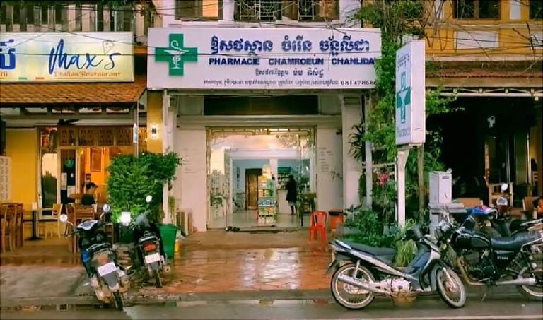 A pharmacy on a street in Kampot, green cross sign above the entrance