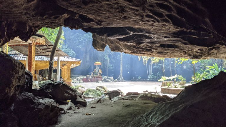 Brick temple shrine inside Phnom Chhnork cave illuminated by a beam of light.